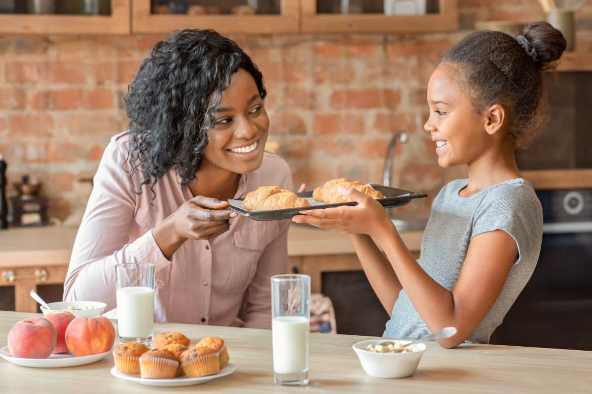 Healthy New Holiday Traditions Mother and daughter sharing breakfast together at kitchen table with pastries and milk.