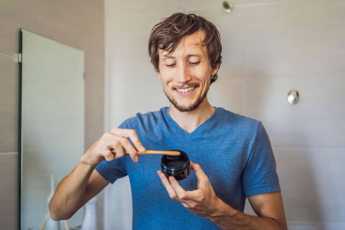 Can You Whiten Your Teeth Naturally Man in blue shirt holding dental floss in bathroom setting, demonstrating proper oral hygiene.